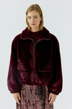 Load image into Gallery viewer, A woman modeling a plush, deep burgundy velvet jacket with a high collar and front pockets, paired with a sparkly mauve sequined skirt, against a light gray studio background.