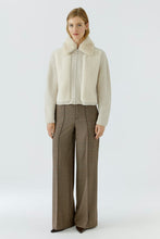 Load image into Gallery viewer, A model stands against a light gray studio background wearing a cream-colored knit zip-up jacket with a faux-fur collar and long sleeves, paired with brown wide-leg trousers.