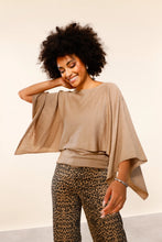 Load image into Gallery viewer, A woman with a large dark curly afro wearing a beige wide-sleeved draped top and leopard print pants, posing against a plain off-white studio background.