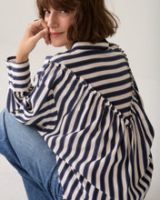 Load image into Gallery viewer, A woman wearing a loose, oversized striped blouse with navy and cream horizontal stripes, paired with blue jeans, photographed against a plain light background.