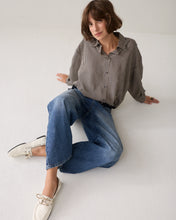 Load image into Gallery viewer, A woman sits on a white floor wearing a brown and white vertically striped button-down shirt, wide-leg blue jeans, and white boat shoes.