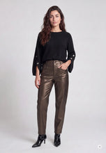 Load image into Gallery viewer, A model stands against a light gray studio background wearing a black long-sleeve top with decorative silver buttons on the cuffs, high-waisted metallic bronze-brown pants, and black pointed-toe ankle boots.