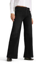 Load image into Gallery viewer, A person wearing black wide-leg jeans with a white long-sleeve shirt tucked in and black pointed shoes, shown from the waist down on a light gray studio background.