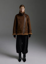 Load image into Gallery viewer, A model stands against a dark gray studio background wearing a brown suede-like jacket with a high collar, asymmetrical zipper, and fuzzy trim, paired with loose black pants and black ankle boots.