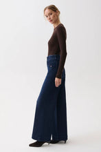 Load image into Gallery viewer, A woman modeling a dark brown long-sleeve top and dark blue wide-leg denim pants against a plain white studio background.