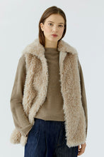 Load image into Gallery viewer, A woman wearing a beige fuzzy faux-fur trimmed cardigan over a taupe knit sweater and dark blue jeans, photographed against a clean light gray studio background.
