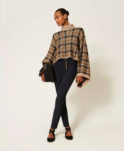 Load image into Gallery viewer, A model stands against a plain light background wearing a beige and black patterned knit sweater with a mock neck and wide bell sleeves, paired with dark navy pants, black shoes, and holding a black handbag.
