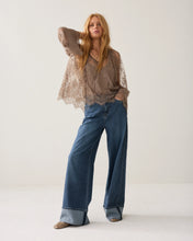 Load image into Gallery viewer, A woman modeling a bohemian-style outfit consisting of a sheer brown lace long-sleeve top and wide-leg blue jeans, standing against a plain off-white studio background.

