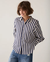 Load image into Gallery viewer, A woman wearing a navy blue and off-white vertically striped button-down shirt with blue jeans, standing against a plain light gray studio background.
