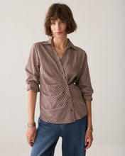 Load image into Gallery viewer, A woman modeling a brown and beige vertically striped wrap shirt with rolled-up sleeves, paired with blue jeans, against a plain light background.
