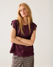 Load image into Gallery viewer, A woman modeling a short-sleeve top in deep burgundy with lace trim on the sleeves and hem, paired with gray plaid trousers, against a plain light gray background.
