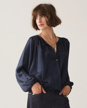 Load image into Gallery viewer, A woman with short brown hair wearing a dark navy blue long-sleeve blouse with a gathered neckline and drawstring, paired with dark denim jeans and gold necklaces, against a plain light gray background.
