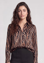 Load image into Gallery viewer, A woman modeling a long-sleeve button-up blouse with a brown and black zebra-like animal print, paired with black pants, against a light gray studio background.
