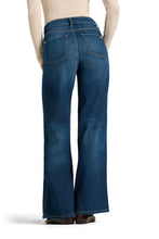 Load image into Gallery viewer, Rear view of a person wearing blue denim jeans with a straight-to-flared leg, paired with a light beige top and brown shoes, on a white studio background.

