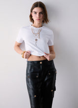 Load image into Gallery viewer, A woman modeling a white short-sleeve crop top and black faux-leather cargo pants with gold-tone hardware, standing against a plain light gray wall.
