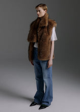 Load image into Gallery viewer, A model wearing a brown fur vest over a white t-shirt and blue jeans, standing against a dark gray studio background.

