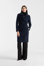Load image into Gallery viewer, A woman modeling a dark navy blue wrap coat with a high collar and tie belt, paired with black wide-leg trousers, against a plain light gray studio background.
