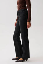 Load image into Gallery viewer, A model wearing black wide-leg flare jeans, a brown long-sleeve top, and dark brown pointed-toe flats, shown from the waist down against a light gray studio background.
