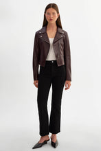 Load image into Gallery viewer, A model stands against a light gray studio background wearing a cropped dark brown leather moto jacket over a white top and black cropped pants.
