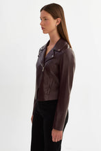 Load image into Gallery viewer, A woman in profile wearing a dark brown leather moto jacket with silver-tone hardware and black pants, photographed against a clean white studio background.
