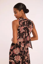 Load image into Gallery viewer, A woman shown from the back wearing a sleeveless black dress with a pink and beige floral paisley print and a sheer bow detail at the neckline, set against a plain light background.
