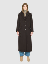 Load image into Gallery viewer, A model wearing a long, dark brown wool-blend coat over a gray turtleneck, blue jeans, and beige ankle boots, shot against a solid light gray background.
